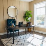 A stylish home office featuring a wooden desk, armchair, and large window with natural light.