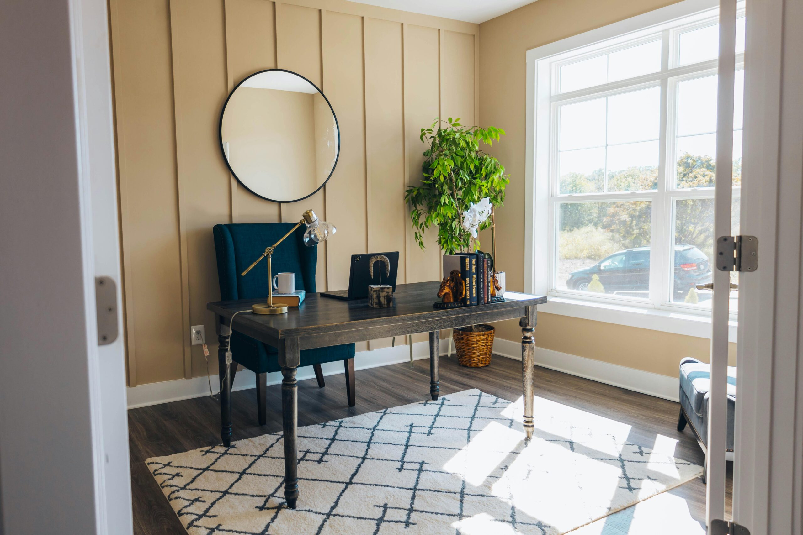 A stylish home office featuring a wooden desk, armchair, and large window with natural light.