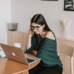 Smiling woman using laptop and earbuds for online learning in a cozy home setting.
