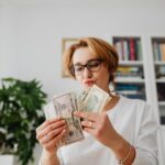 Woman with eyeglasses counting dollar bills in a home setting
