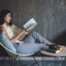 A young woman sits comfortably in a chair reading a book for relaxation.