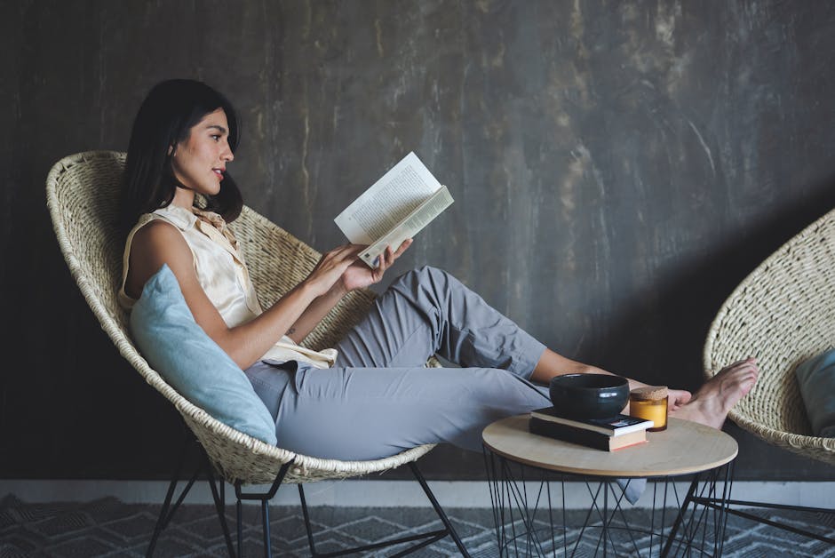 A young woman sits comfortably in a chair reading a book for relaxation.