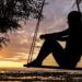 A serene sunset silhouette of a woman sitting on a swing by the seashore, evoking tranquility and reflection.